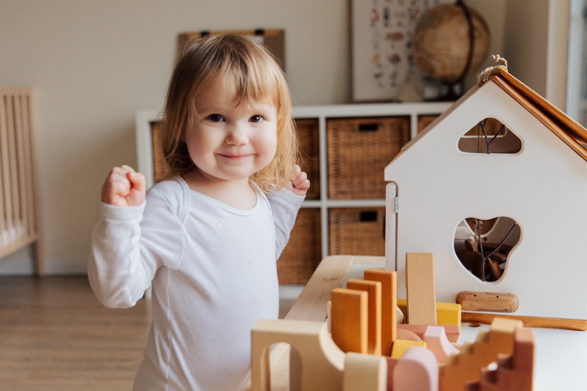 A toddler choosing toys from a low open shelf in a tidy, calm playroom